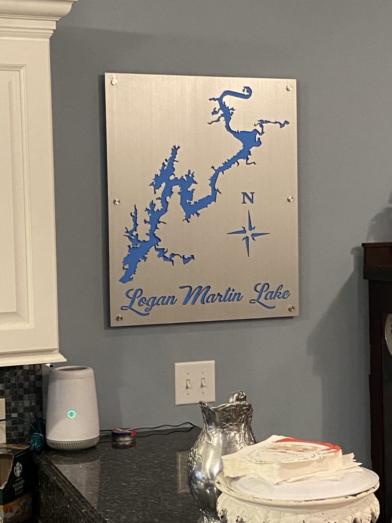 Logan Martin Lake map with blue cutout and compass rose on brushed metal, mounted on a kitchen wall above a counter.