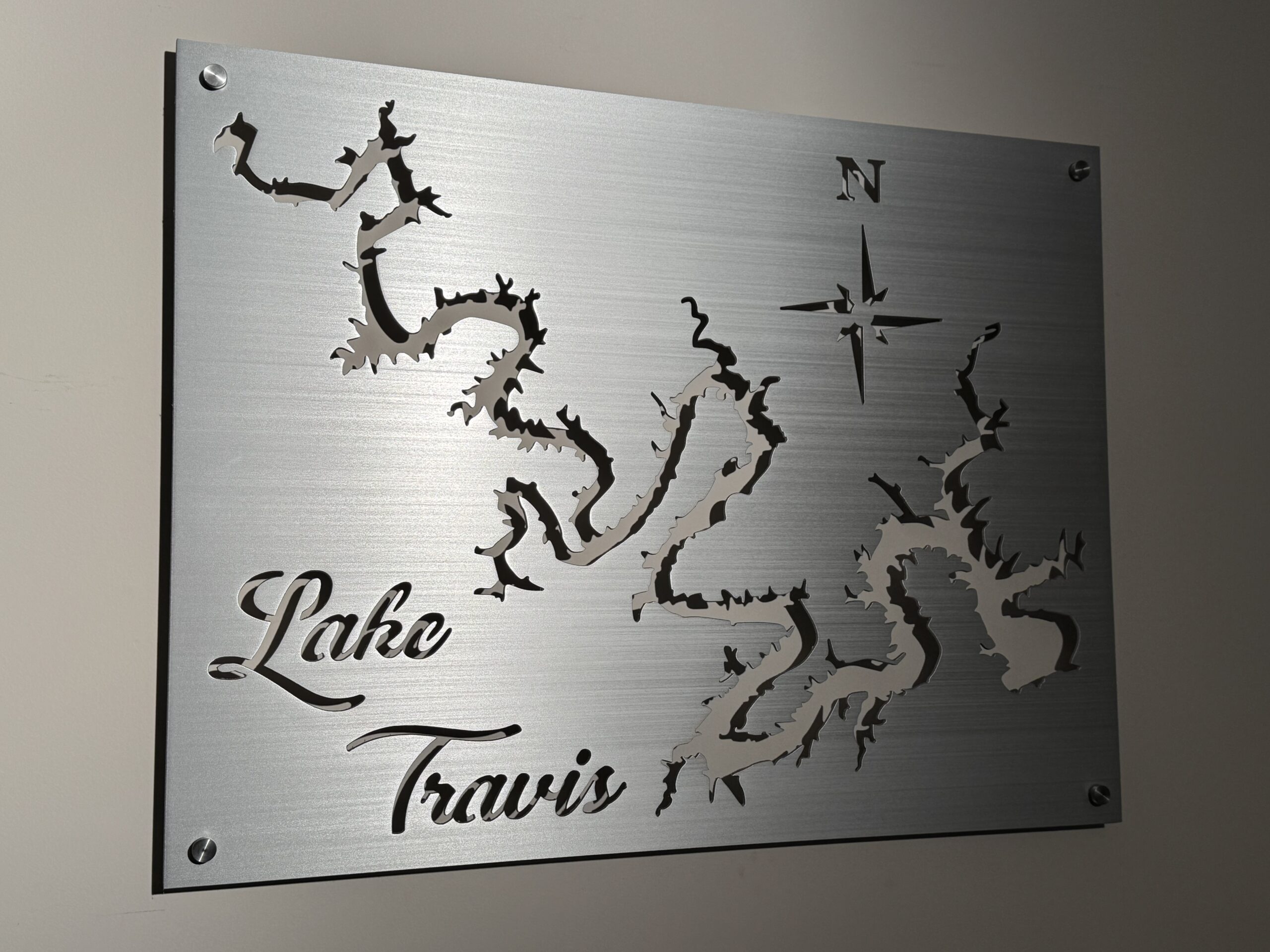 Metal wall art of Lake Travis with intricate cutout design and compass rose, mounted on a light-colored wall.